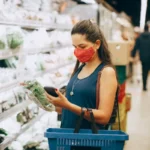 Seorang wanita sedang berbelanja kebutuhan pokok di supermarket sambil mengecek harga produk